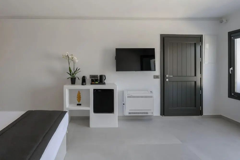 Helles Hotelzimmer mit wandmontiertem Fernseher, Minibar, Kaffeestation und dunkler Eingangstür.