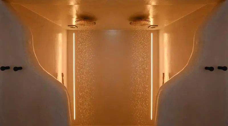 Zwei Regenduschen mit fließendem Wasser und beleuchteten Wänden im Badezimmer.