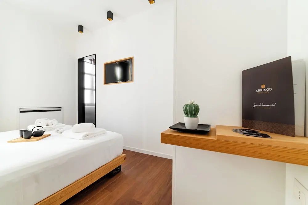 Helles Hotelzimmer mit Doppelbett, Parkettboden, Flachbildfernseher und kleiner Topfpflanze.