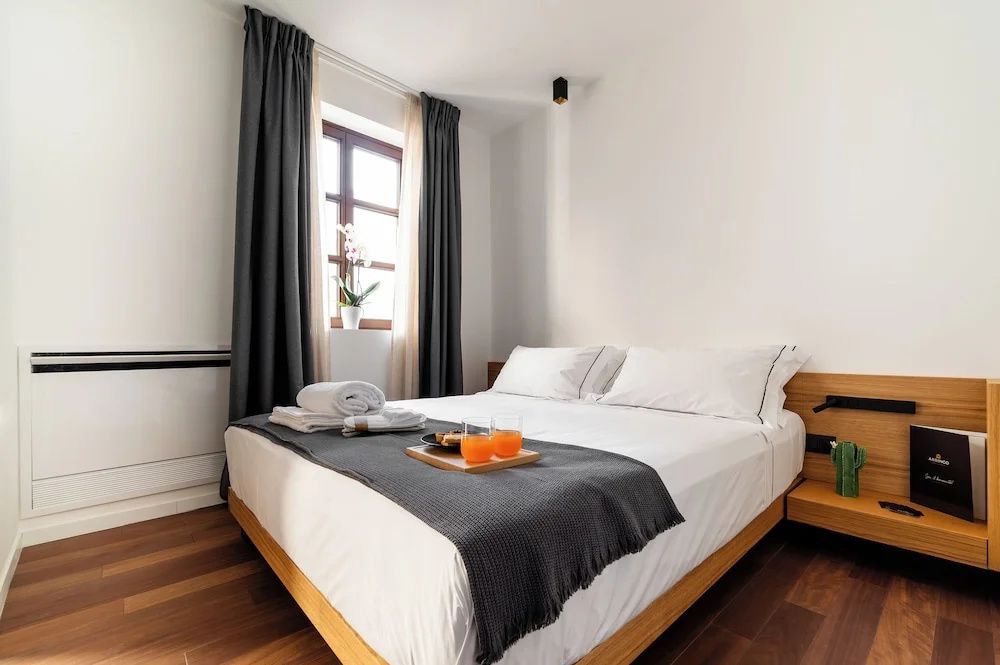 Doppelbett mit weißer Bettwäsche, grauer Tagesdecke, Handtüchern und Serviertablett.