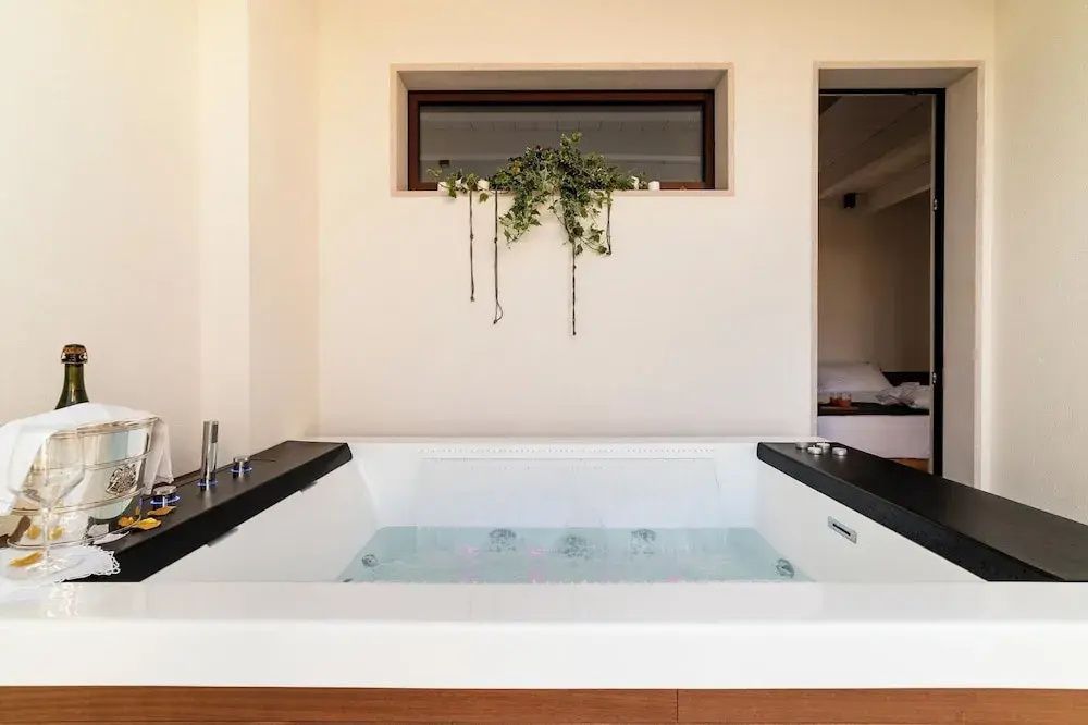 Weißer Whirlpool mit gefülltem Wasser unter einem kleinen Fenster mit Pflanze.