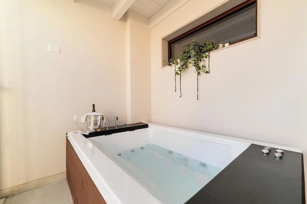 Moderner Whirlpool mit Sektkühler am Rand unter einem schmalen Fenster.