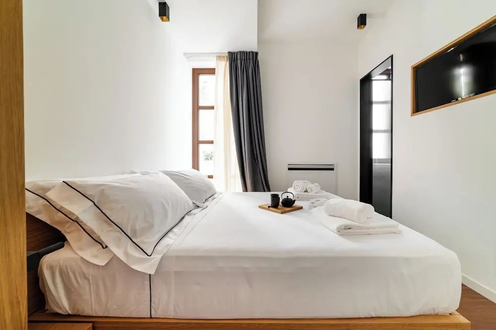 Doppelbett mit weißem Bezug, gefalteten Handtüchern und Teekanne auf dem Tablett.