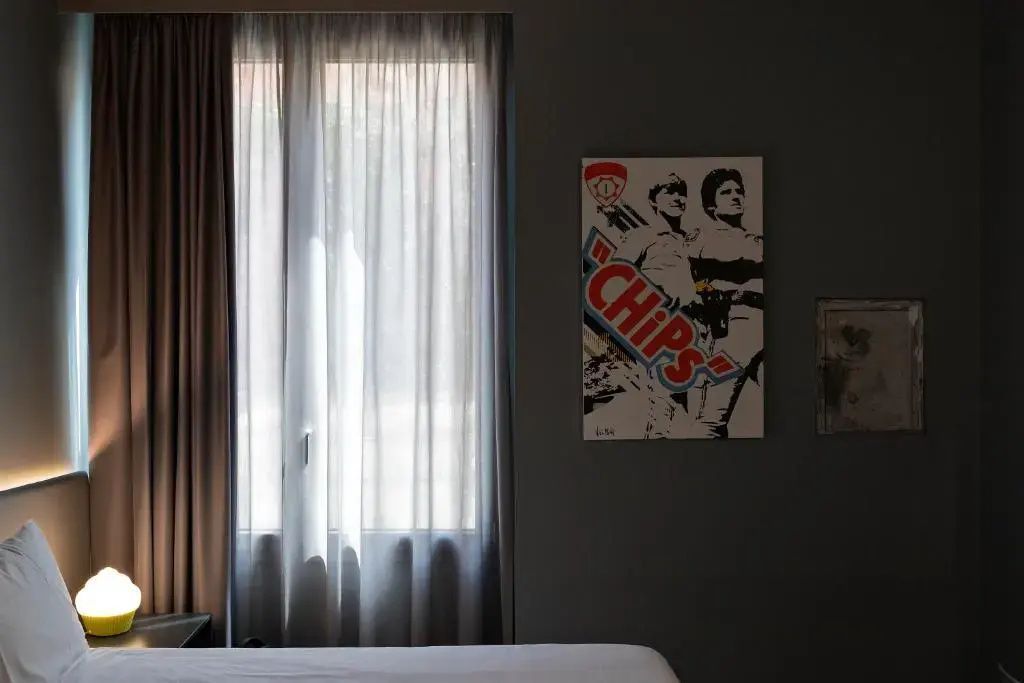 Fenster mit transparentem Vorhang und Wand mit Pop-Art-Bild im Hotelzimmer.