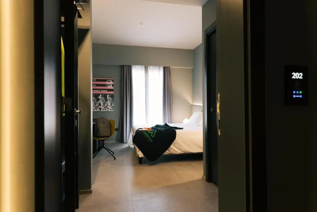 Blick durch den Flur in ein moderner gestaltetes Hotelzimmer mit Doppelbett und Schreibtisch.
