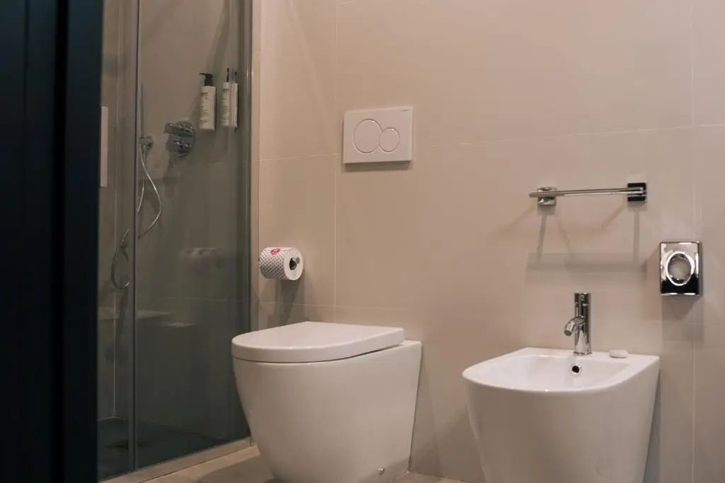 Badezimmerbereich mit Toilette, Bidet und einer Dusche hinter Glas.