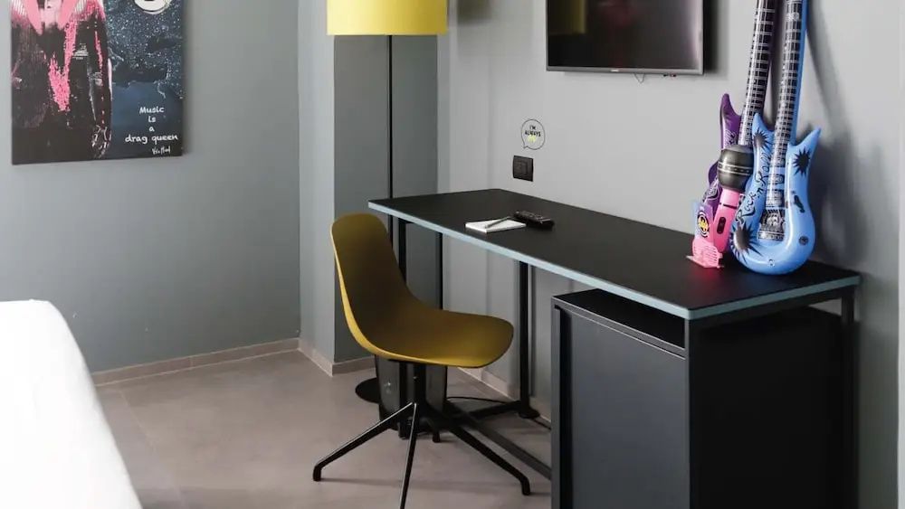 Arbeitsbereich im Hotelzimmer mit schwarzem Tisch, gelbem Stuhl und Stehlampe.