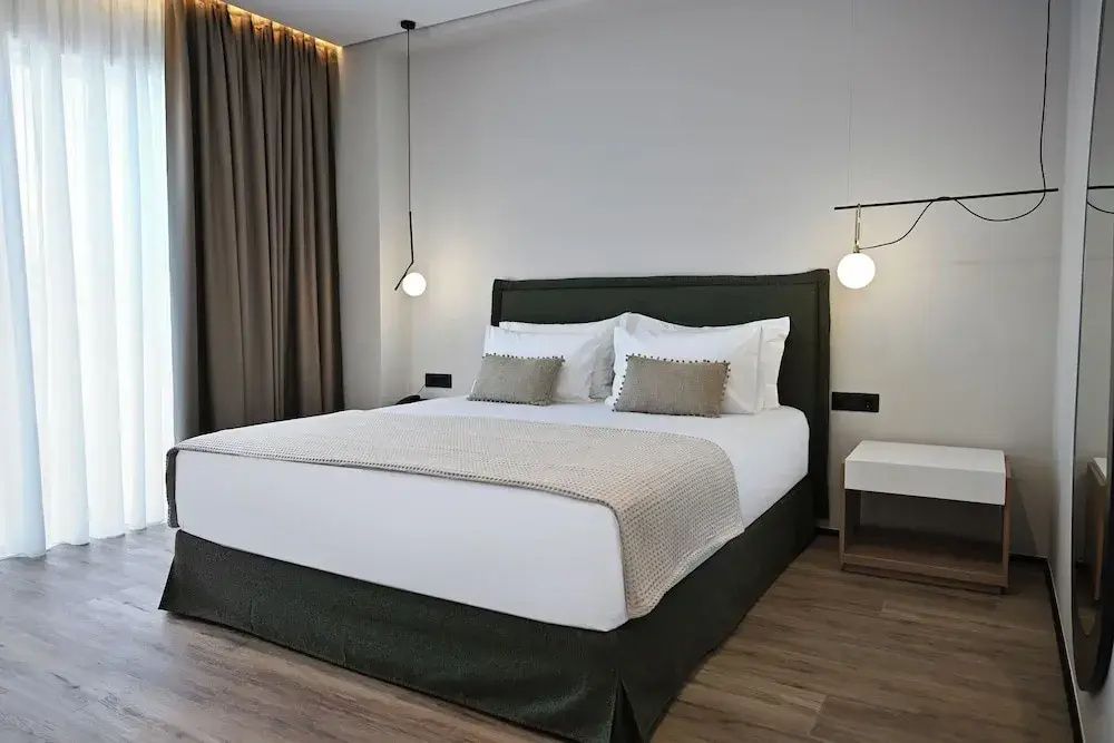 Doppelbett mit dunkelgrünem Kopfteil, weißer Bettwäsche und modernen Kugelleuchten.