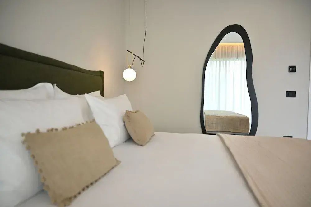 Doppelbett mit Kissen und ein großer, geschwungener Spiegel im modernen Hotelzimmer.