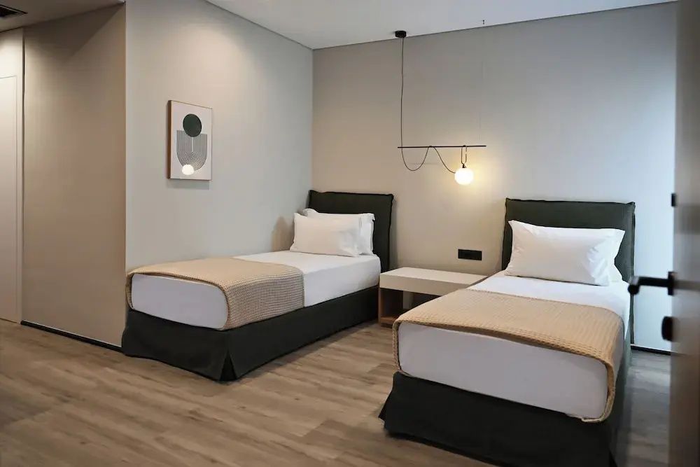 Zwei Einzelbetten mit weißer Bettwäsche und dunkelgrünen Kopfteilen im hellen Zimmer.