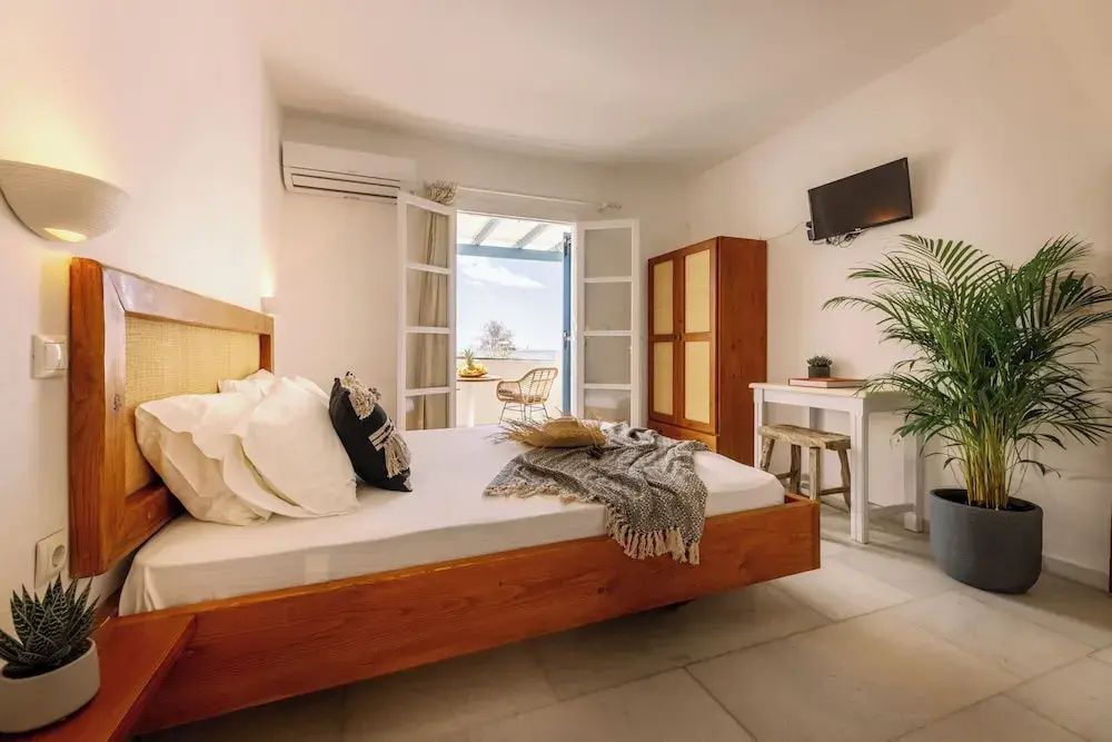 Helles Studio mit Holzdoppelbett, Kleiderschrank und Blick auf den Balkon.