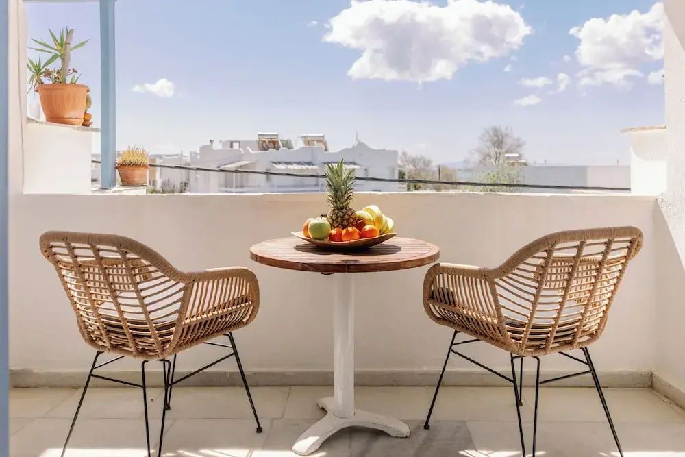 Balkon mit zwei Stühlen aus Geflecht, Obstschale auf dem Tisch und Blick auf Häuser.
