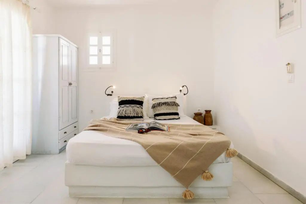 Hell eingerichtetes Schlafzimmer mit weißem Doppelbett, beiger Tagesdecke und einem weißen Kleiderschrank.