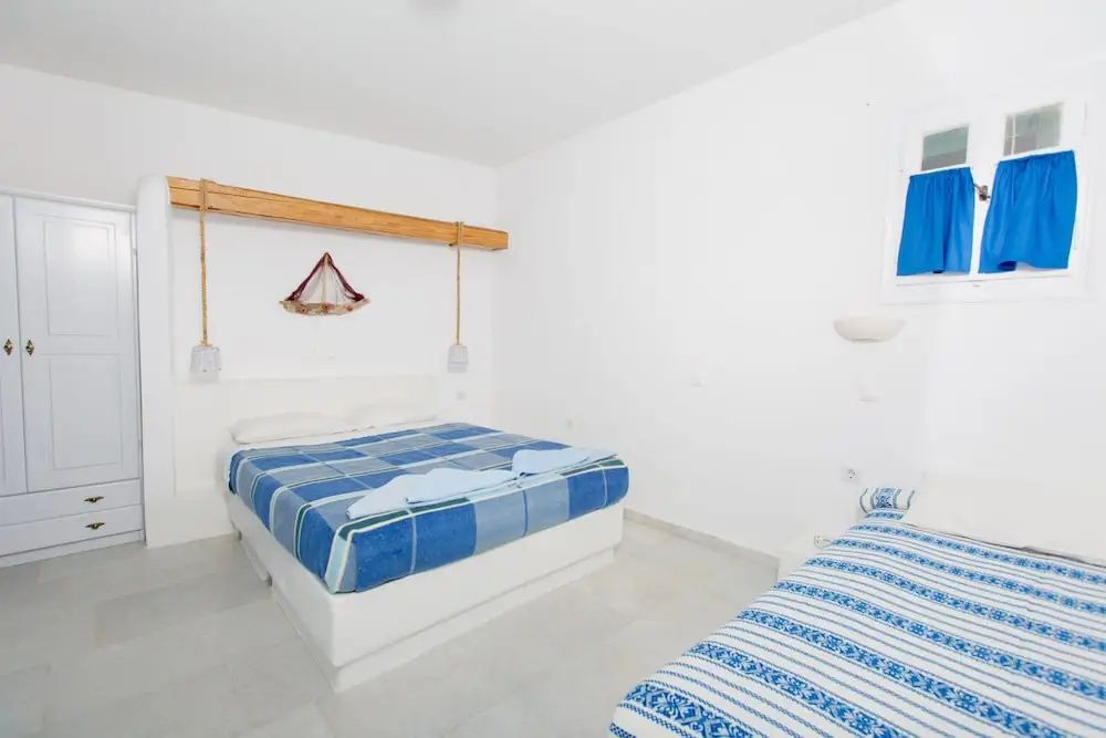 Schlafzimmer mit weiß getünchten Wänden sowie Doppelbett und Einzelbett mit blauer Wäsche.