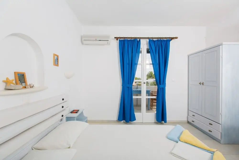 Weiß gestaltetes Schlafzimmer mit Doppelbett, blauen Vorhängen und Balkontür.