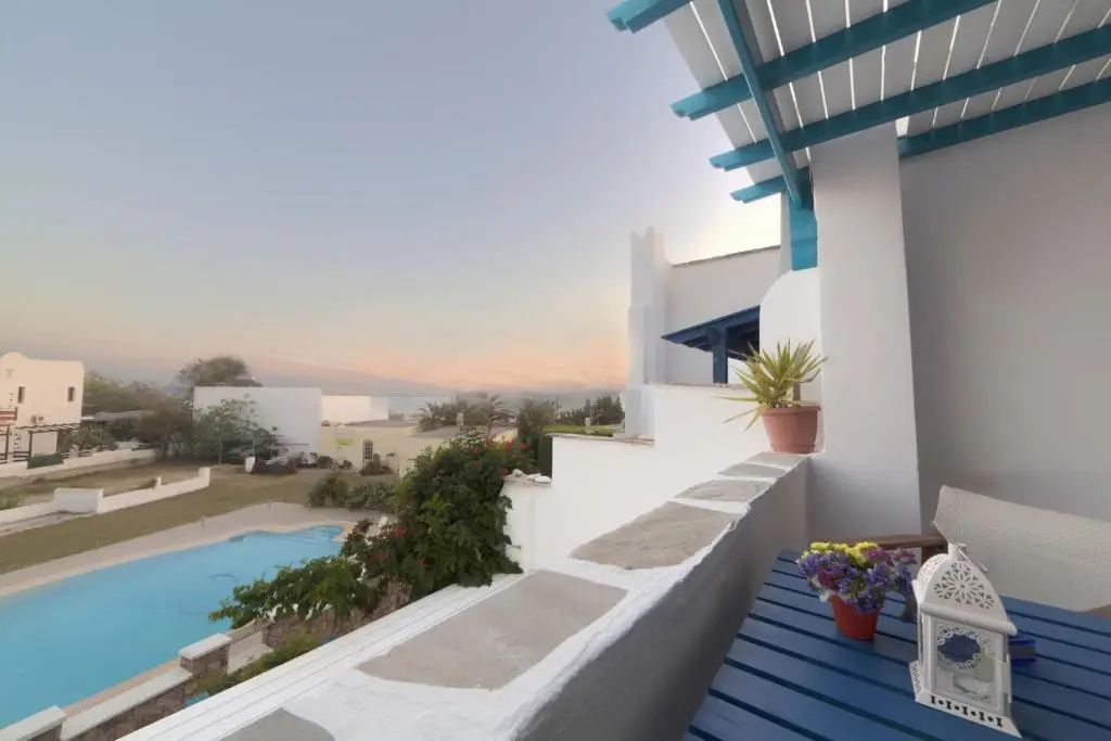 Blick vom Balkon mit blauem Holztisch auf den Swimmingpool und die Hügellandschaft.