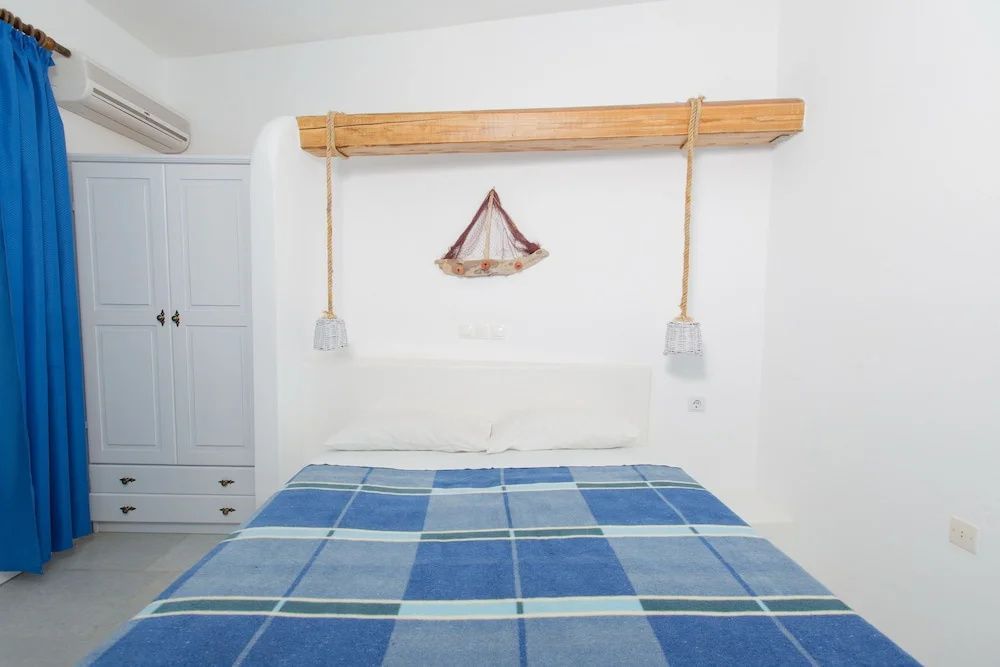 Doppelbett mit blau karierter Decke vor weißer Wand unter einer Holzdekoration.