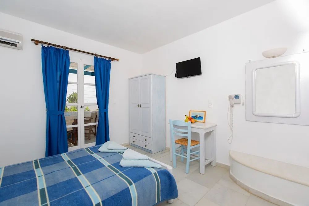 Helles Hotelzimmer mit blau kariertem Bett, weißem Schrank und Schreibtisch mit blauem Stuhl.
