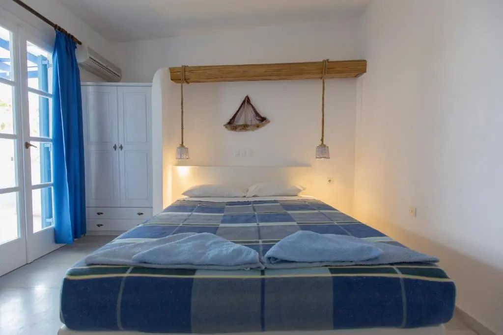 Doppelbett mit blau karierter Tagesdecke unter einem dekorativen Holzbalken an der Wand.
