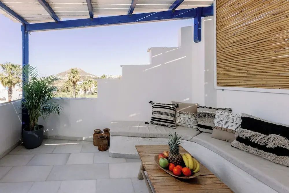 Überdachte Terrasse mit Eckbank, Kissen, Holztisch mit Obstschale und Blick in die Umgebung.