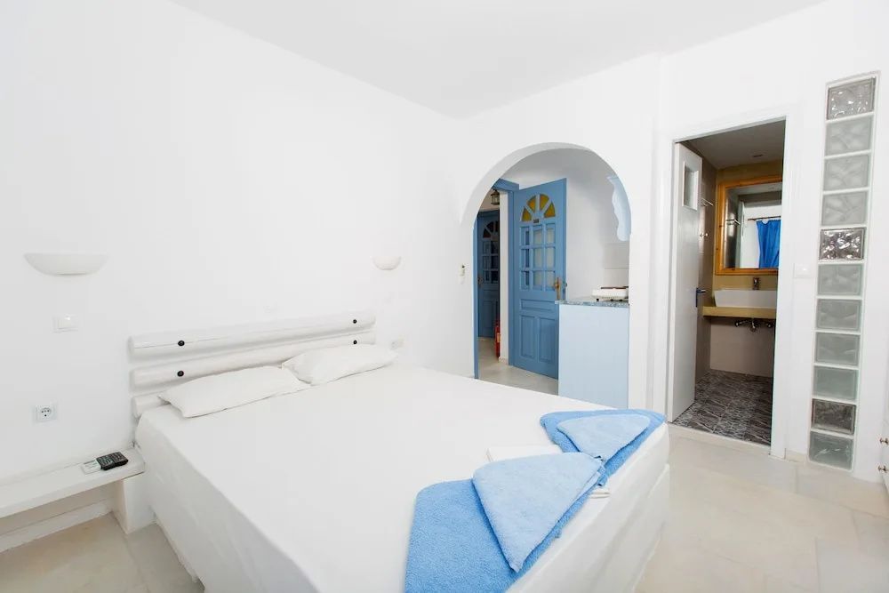 Weiß eingerichtetes Schlafzimmer mit Doppelbett, blauen Handtüchern und Blick auf einen Rundbogen.