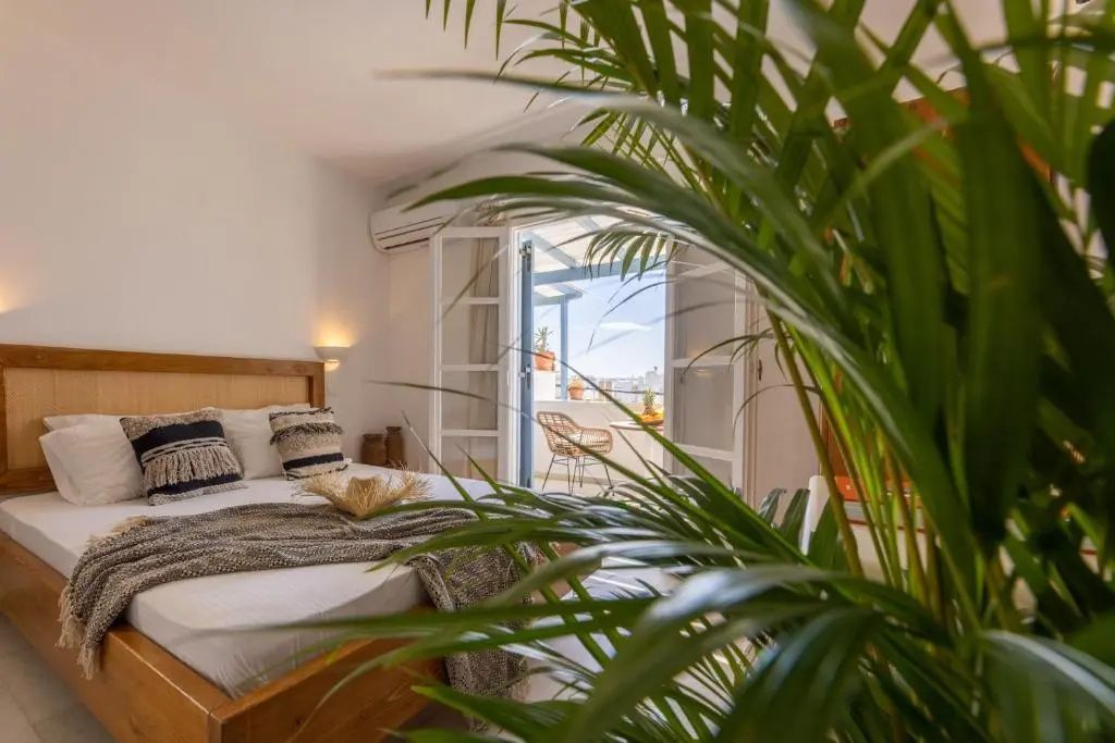 Helles Schlafzimmer mit Holzbett und Blick durch die geöffnete Balkontür.