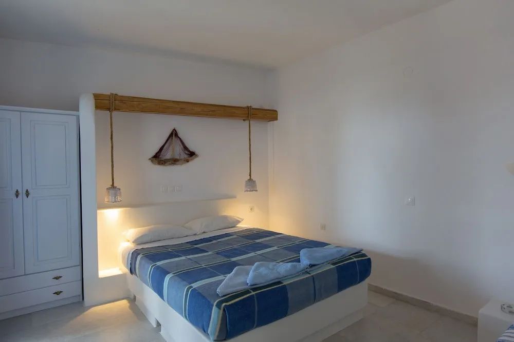 Schlafzimmer mit blau karierter Bettdecke, indirekter Beleuchtung und Holzdeko an der Wand.