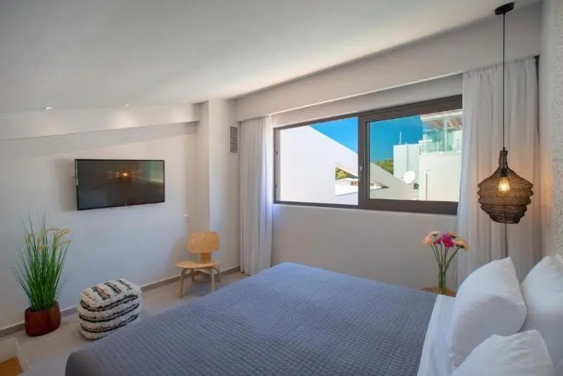 Helles Schlafzimmer mit Doppelbett, Wandfernseher und Fensterblick.