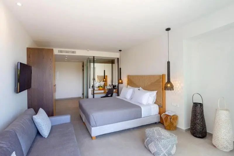 Modernes Hotelzimmer mit Doppelbett, beigefarbenem Kopfteil und grauer Couch.