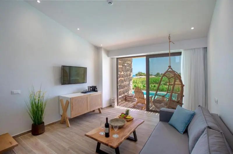 Wohnbereich einer Suite mit Couch, Holztisch, Fernseher und Terrassenausgang zum Pool.