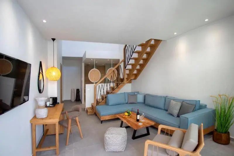 Wohnbereich einer Suite mit hellblauem Ecksofa, Holztisch und einer Holztreppe ins Obergeschoss.