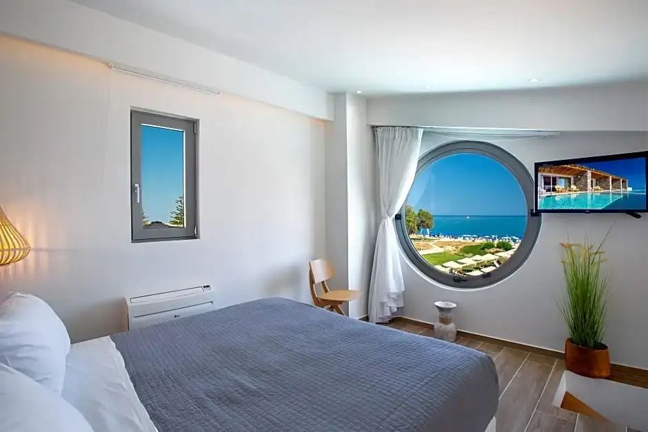 Schlafzimmer mit Doppelbett und rundem Fenster mit Blick auf den Strand und das Meer.