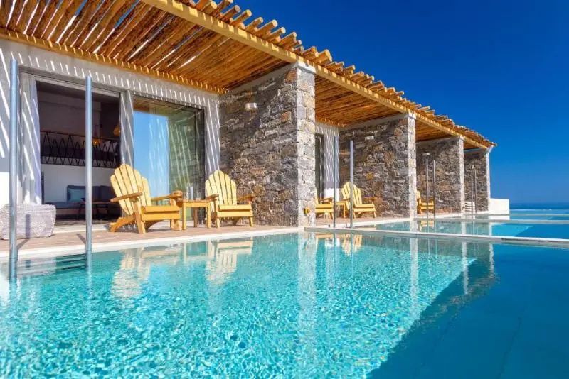 Terrasse mit Steinmauer, Holzdach und Holzstühlen direkt an einem Privatpool.