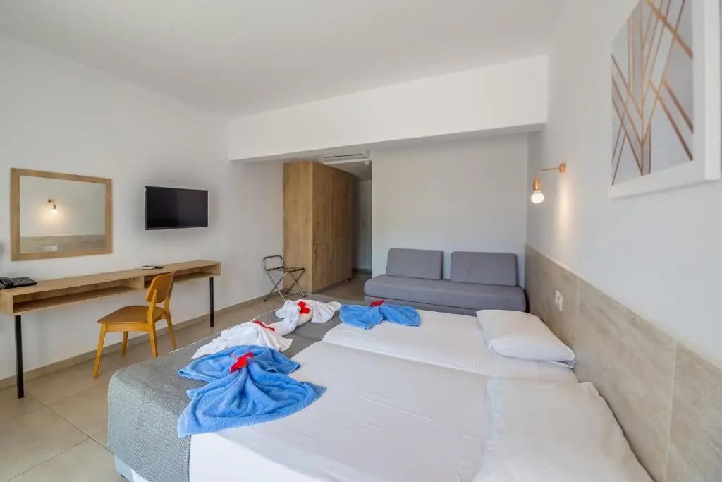 Hell eingerichtetes Hotelzimmer mit Doppelbett, grauem Sofa und Schreibtisch