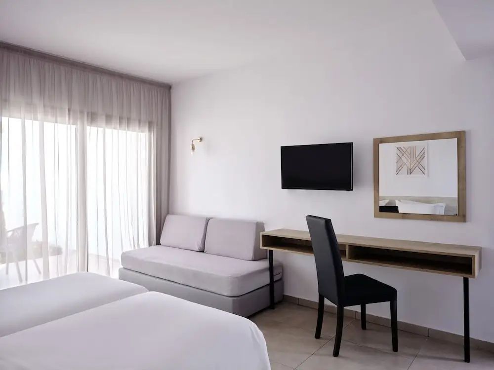 Hell eingerichtetes Hotelzimmer mit Schlafsofa, Schreibtisch, Fernseher und Balkonzugang.