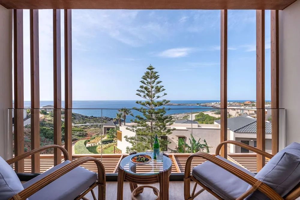 Blick vom Balkon mit zwei Sesseln und einem Tisch auf die Küste und das Meer.