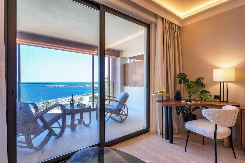 Blick durch eine grosse Glas-Schiebetür im Zimmer auf den Balkon und das Meer.