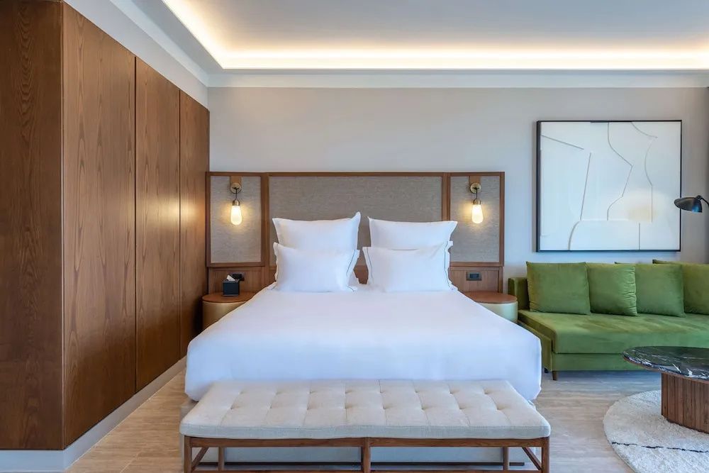 Doppelbett mit weisser Bettwäsche, Holzverkleidung und Sitzbank im Hotelzimmer.
