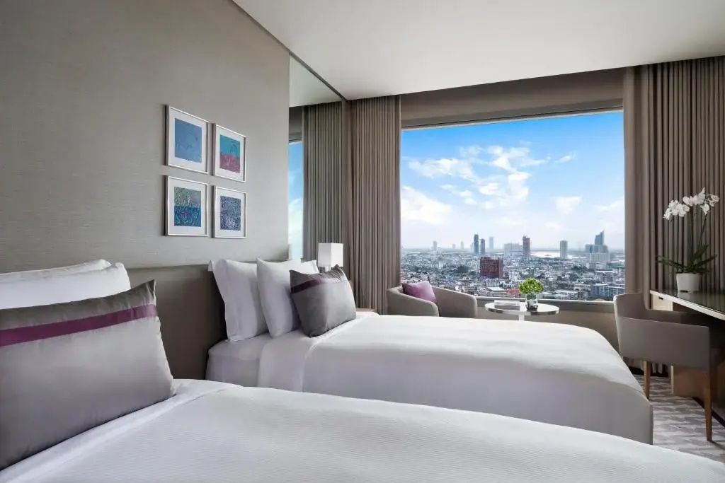 Zwei Betten in einem Hotelzimmer mit Panoramablick durch das Fenster auf die Stadt.