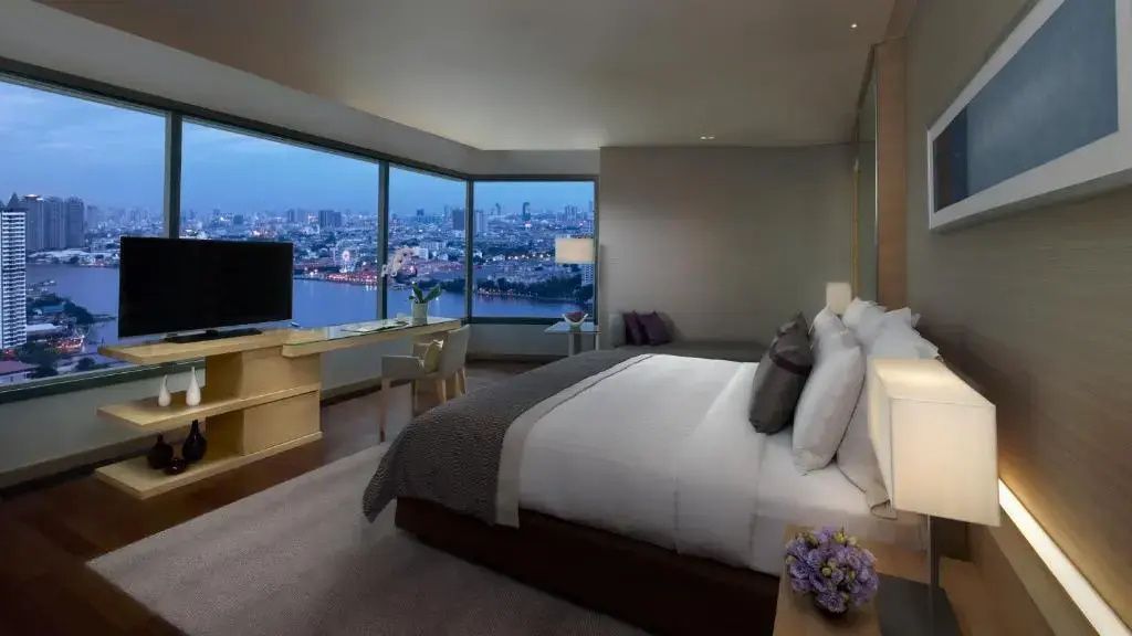 Hotelzimmer bei Dämmerung mit Blick durch große Fenster auf die beleuchtete Stadt.