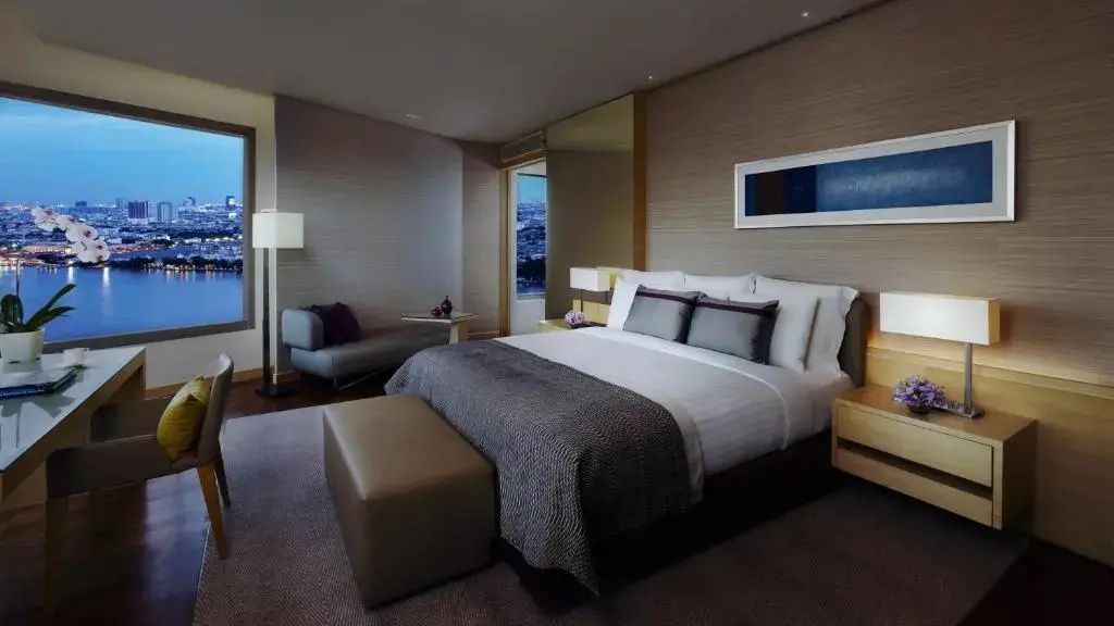 Doppelbett in modern gestaltetem Hotelzimmer mit Sitzgelegenheit und Wandbild.
