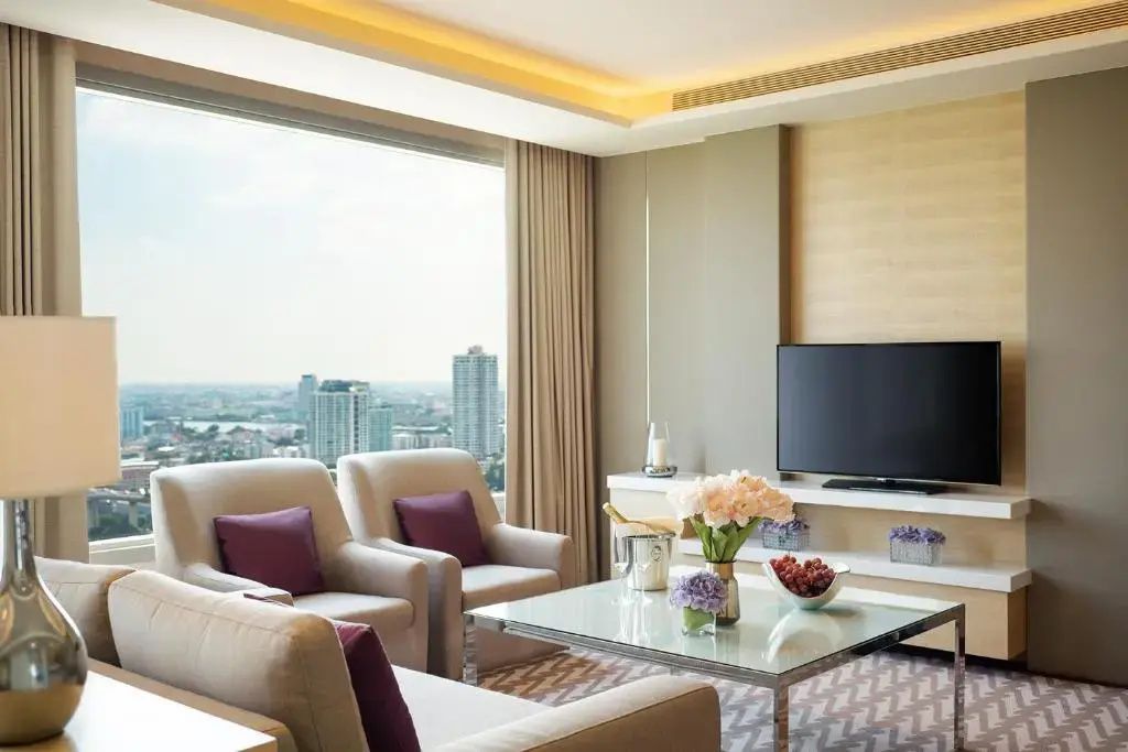 Sitzbereich einer Suite mit Sesseln, Couchtisch und Blick durch das Fenster auf die Stadt.
