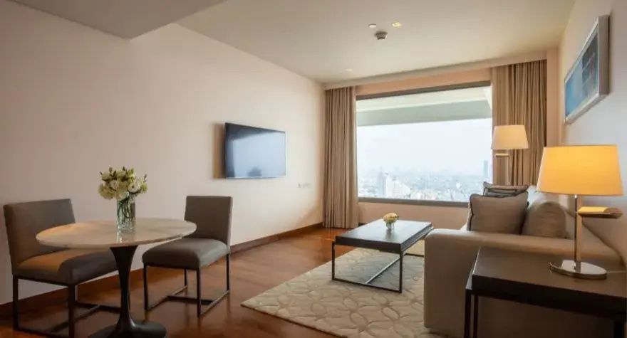 Wohnbereich eines Hotelzimmers mit Sofa, Couchtisch, Wand-TV und großem Fenster.