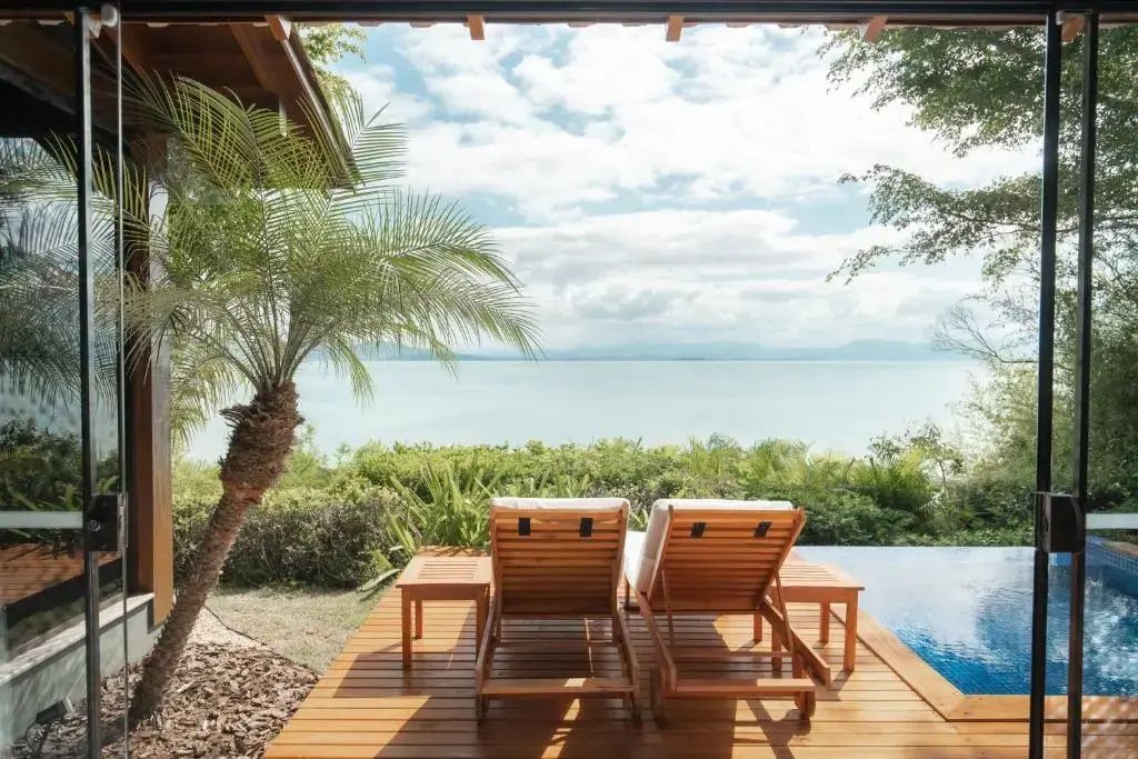 Zwei Sonnenliegen aus Holz auf einer Terrasse mit Blick auf das Meer.