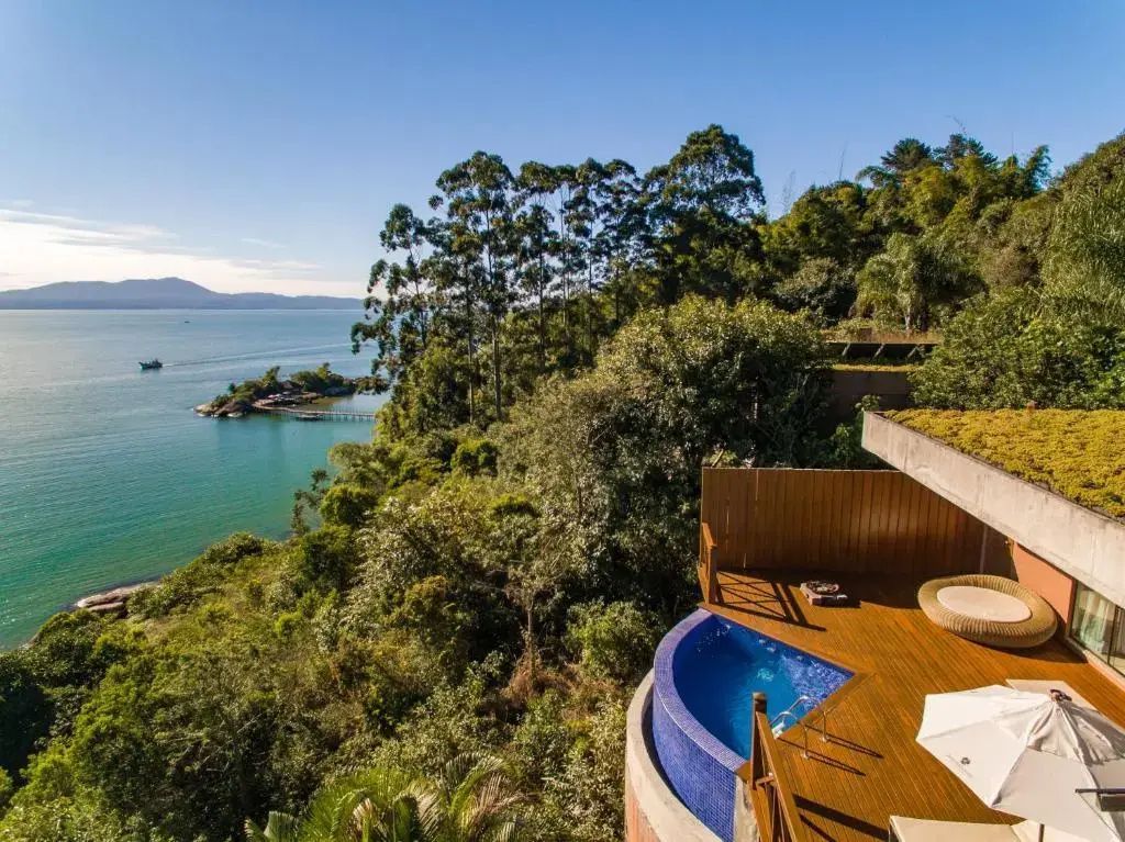 Holzdeck mit rundem blauem Pool und Blick auf das Meer und grüne Küstenlandschaft.