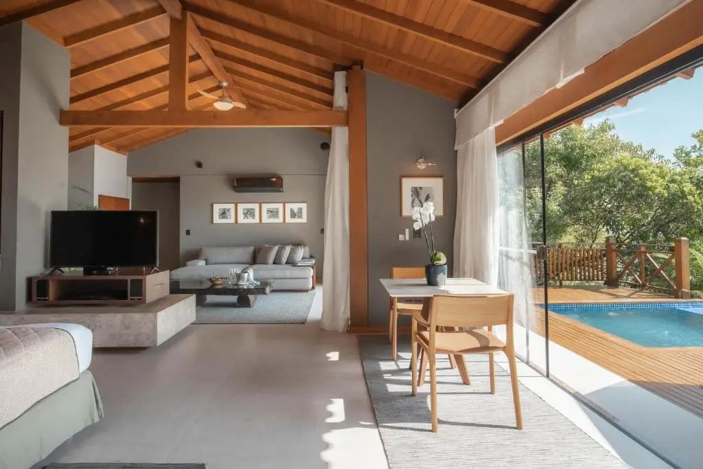 Offener Wohnbereich mit Holzdecke, Esstisch, grauem Sofa und Blick auf den Pool.