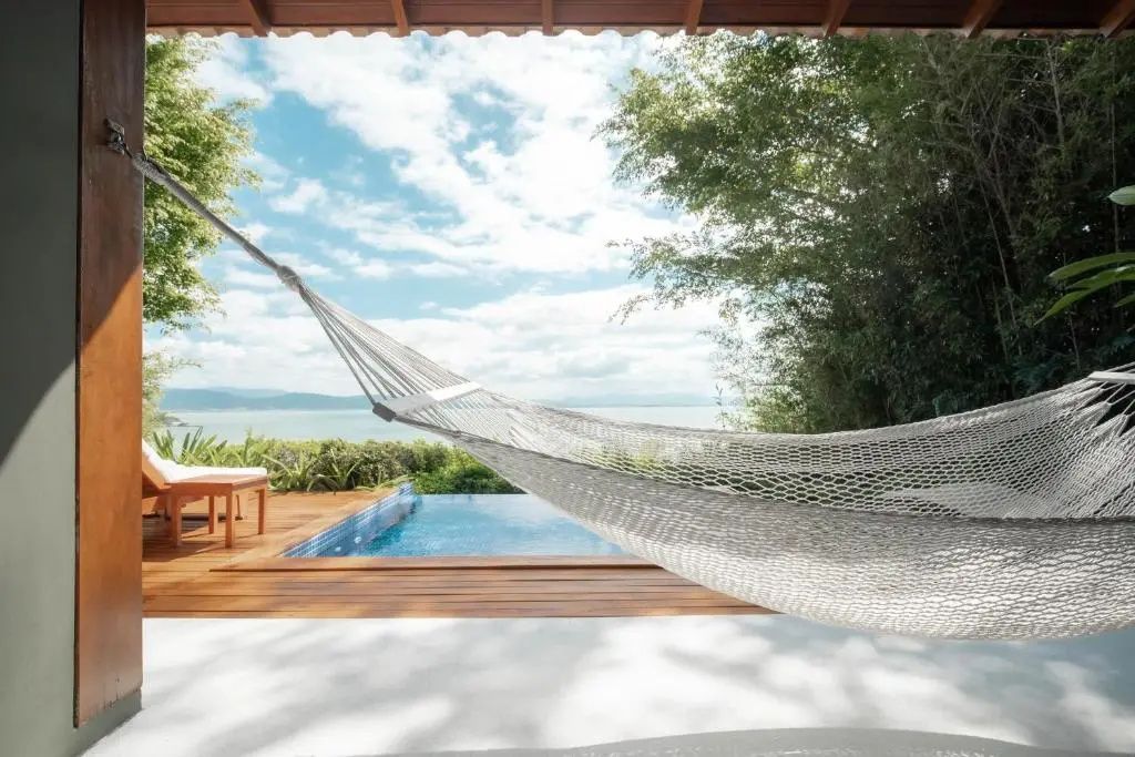 Hängematte auf einer Terrasse mit Blick auf den Pool und das Meer im Hintergrund.