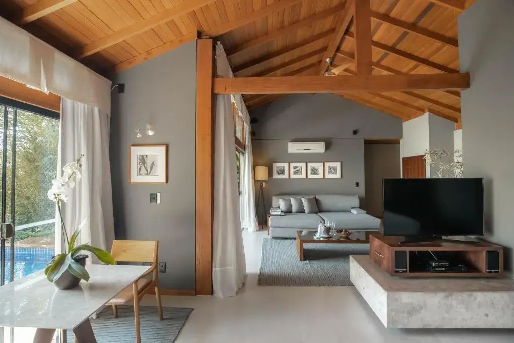 Wohnzimmer einer Suite mit Holzgebälk, grauem Sofa und Esstisch.