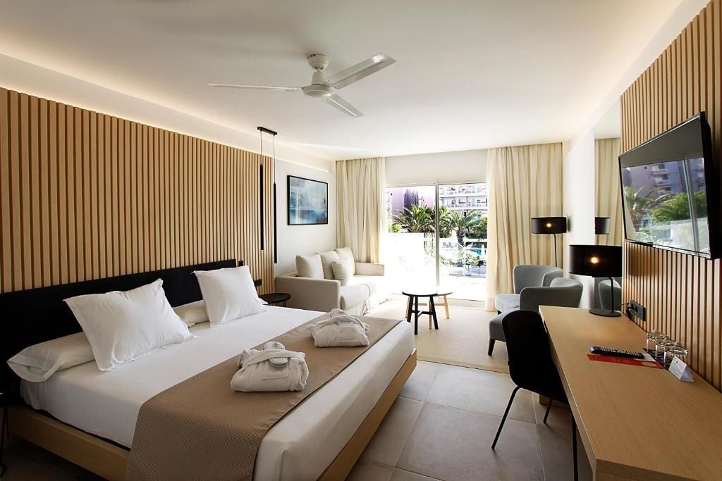 Helles Hotelzimmer mit Doppelbett, Sitzecke mit Sofa und Zugang zum Balkon.