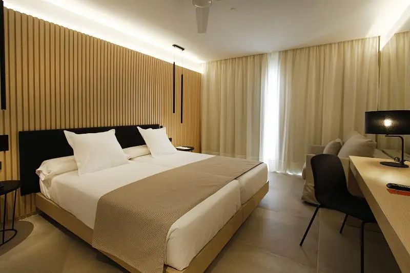 Helles Hotelzimmer mit Holzlamellen an der Wand, Doppelbett und beigen Vorhängen